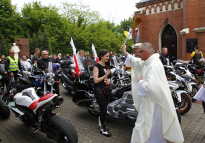 Zdjęcie księdza proboszcza święcącego uczestników oraz motocykle stojące przed kościołem pw. Niepokalanego Poczęcia NMP w Koluszkach