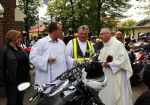 Zdjęcie księdza proboszcza oraz uczestników VIII Koluszkowskiego Zlotu Motocyklowego stojących przed kościołem pw. Niepokalanego Poczęcia NMP w Koluszkach