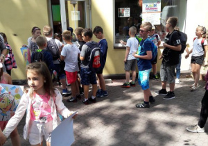 Zdjęcie uczestników II turnusu "Wakacji w mieście" biorących udział w warsztatach edukacyjnych "Uwolnij Wyobraźnię" inspirowanych sztuką Katarzyny Kobro i Władysława Strzemińskiego prowadzonych przez Mateusza Jaśkiewicza przed Salą Muzealną MOK