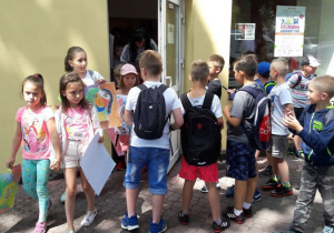 Zdjęcie uczestników II turnusu "Wakacji w mieście" biorących udział w warsztatach edukacyjnych "Uwolnij Wyobraźnię" inspirowanych sztuką Katarzyny Kobro i Władysława Strzemińskiego prowadzonych przez Mateusza Jaśkiewicza przed Salą Muzealną MOK