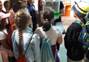 Zdjęcie pani oprowadzącej oraz uczestników wyjazdu do Centrum Nauki Experymentarium w Manufakturze w ramach II turnusu "Wakacji w mieście" podczas zwiedzania obiektu