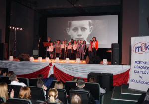 Zdjęcie wystepujących na scenie podczas koncertu patriotycznego pt. Tobie Ojczyzno w Miejskim Ośrodku Kultury w Koluszkach