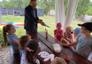 Zdjęcie przedstawia uczestników I turnusu Wakacji w mieście oraz gościa specjalnego - Burmistrza Koluszek Waldemara Chałata wręczającego dzieciom słodkie upominki - czekolady.