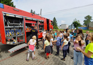 Zdjęcie przedstawia uczestników drugiego turnusu Wakacji w Mieście 2021 oglądających wnętrze wozu strażackiego prezentowanego przez strażaków PSP