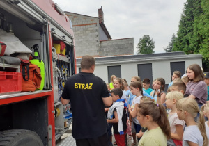 Zdjęcie przedstawia uczestników drugiego turnusu Wakacji w Mieście 2021 oglądających wnętrze wozu strażackiego prezentowanego przez strażaków PSP