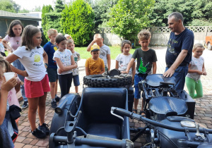 Zdjęcie przedstawia uczestników II turnusu słuchających ciekawostek o zabytkowym motorze, którym wożone były dzieci po okolicy Zalesia