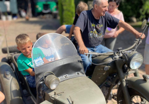 Zdjęcie przedstawia uczestników II turnusu Wakacji w mieście oraz Pana Pawła Swęda siedzących w koszu i na motocyklu podczas wizyty w Zalesiu.