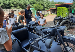 Zdjęcie przedstawia uczestników II turnusu słuchających ciekawostek o zabytkowym motorze, którym wożone były dzieci po okolicy Zalesia