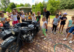 Zdjęcie przedstawia uczestników II turnusu słuchających ciekawostek o zabytkowym motorze, którym wożone były dzieci po okolicy Zalesia