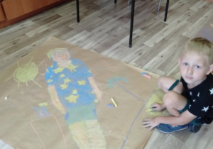 Zdjęcie przedstawia uczestnika warsztatów plastycznych MOK prezentującego pracę przygotowaną na mural "Mój kolorowy dzień"