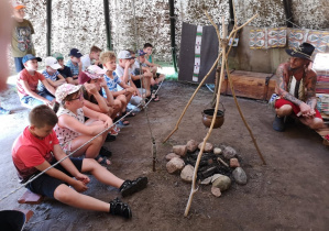 Zdjęcie przedstawia uczestników II turnusu Wakacji w mieście podczas warsztatów w wiosce indiańskiej TATANKA. Dzieci znajdują się w wigwamie indiańskim i słuchają opowieści o tradycjach i kulturze indiańskiej.