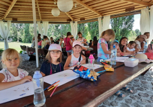 Zdjęcie przedstawia uczestników II turnusu Wakacji w mieście podczas zajęc plastycznych. Dzieci wykonują maski oraz kolorują obrazki ze zwierzętami