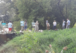 Zdjęcie przedstawia instruktora oraz uczestników artystycznego pleneru malarskiego w ramach warsztatów "Animacje na wakacje" podczas malowania prac w Lisowicach