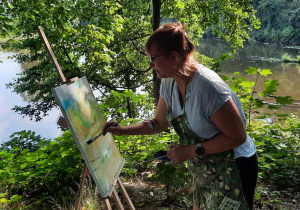 Zdjęcie przedstawia uczestniczkę artystycznego pleneru malarskiego w ramach warsztatów "Animacje na wakacje" podczas malowania prac w Lisowicach