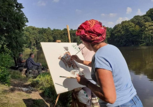 Zdjęcie przedstawia uczestniczkę artystycznego pleneru malarskiego w ramach warsztatów "Animacje na wakacje" podczas malowania prac w Lisowicach