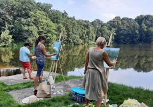 Zdjęcie przedstawia uczestników artystycznego pleneru malarskiego w ramach warsztatów "Animacje na wakacje" podczas malowania prac w Lisowicach