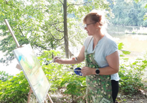 Zdjęcie przedstawia uczestniczkę artystycznego pleneru malarskiego w ramach warsztatów "Animacje na wakacje" podczas malowania prac w Lisowicach