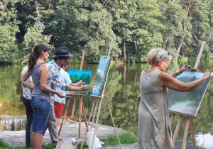 Zdjęcie przedstawia instruktora oraz uczestników artystycznego pleneru malarskiego w ramach warsztatów "Animacje na wakacje" podczas malowania prac w Lisowicach