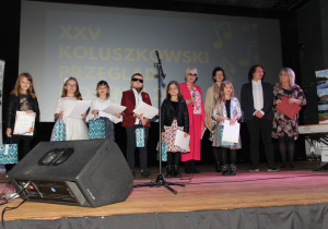 Zdjęcie przedstawia Jury, Dyrektor MOK oraz laureatów XXV Koluszkowskiego Przeglądu Piosenki w kategorii szkoły podstawowe klasy I – III