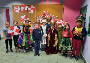 Zdjęcie przedstawia uczestników warsztatów patriotycznych „Polska znana i mniej znana” przebranych w stroje z dawnych czasów oraz prezentującyh prace plastyczne powstałe podczas warsztatów