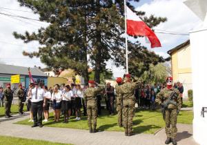 Zdjęcie asysty wojskowej oraz uczestników podczas wciągania flagi państwowej na maszt w ramach Uroczystych Obchodów 231 Rocznicy Uchwalenia Konstytucji 3 Maja przy Pomniku Orła Białego w Koluszkach