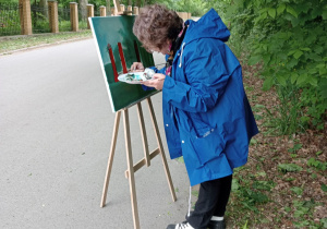 Zdjęcie przedstawia uczestniczkę II artystycznego pleneru malarskiego w Lisowicach podczas malowania pracy