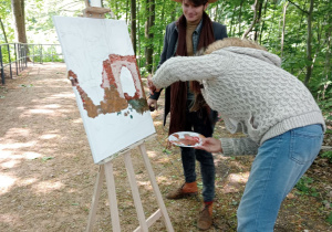 Zdjęcie przedstawia instrukotra Mateusza Jaskiewicza oraz uczestniczkę II artystycznego pleneru malarskiego w Lisowicach podczas malowania pracy